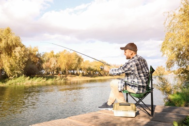 Photo of Man with rod fishing on wooden pier at riverside. Recreational activity