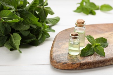 Photo of Bottles of essential oil and mint on white wooden table