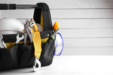 Photo of Black bag with construction tools on white wooden table. Space for text