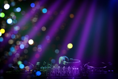 Image of Modern DJ controller and headphones under beams of light in night club, bokeh effect