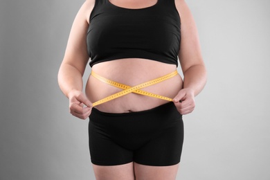 Photo of Fat woman with measuring tape on grey background, closeup. Weight loss