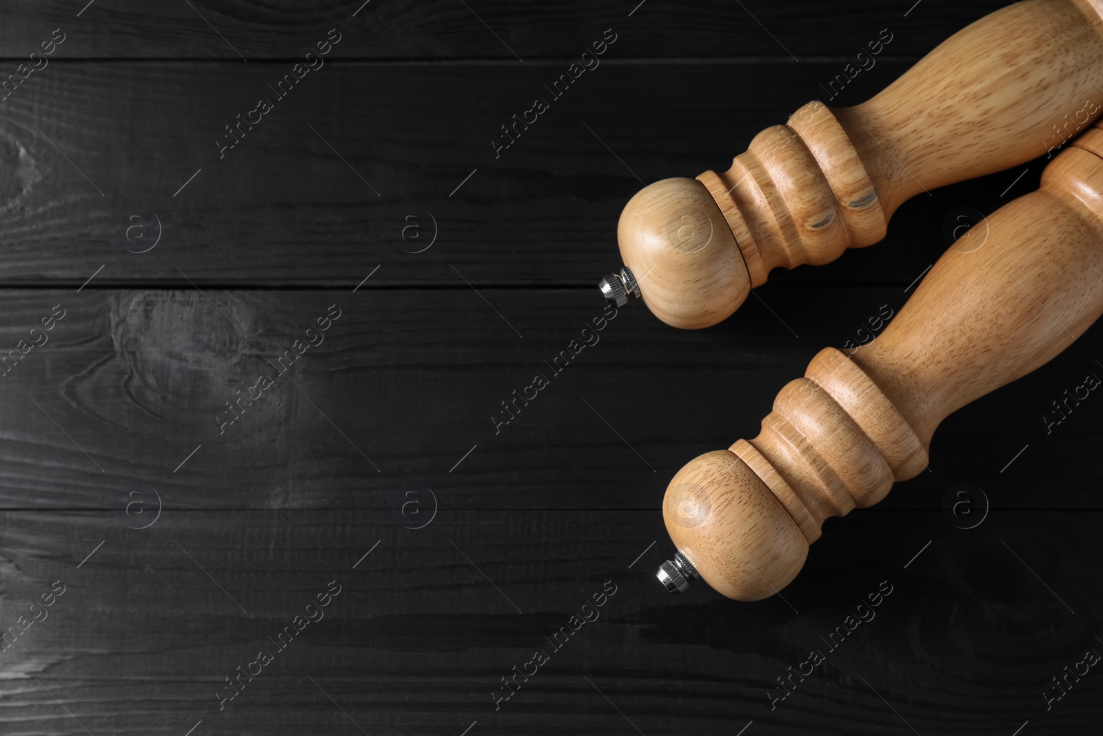 Photo of Salt and pepper shakers on black wooden table, flat lay. Space for text