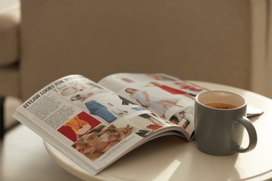 Fashion magazine and cup of hot drink on white table indoors