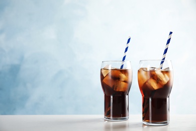 Glasses of refreshing cola with ice cubes and straws on table. Space for text