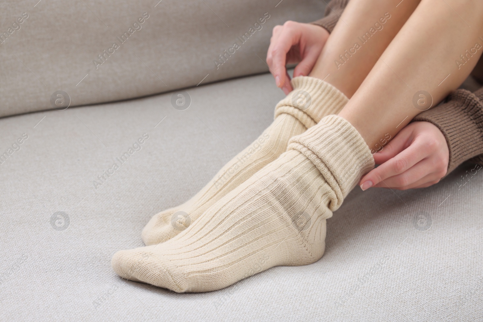 Photo of Woman in warm socks on sofa at home, closeup. Space for text