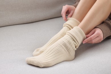 Woman in warm socks on sofa at home, closeup. Space for text