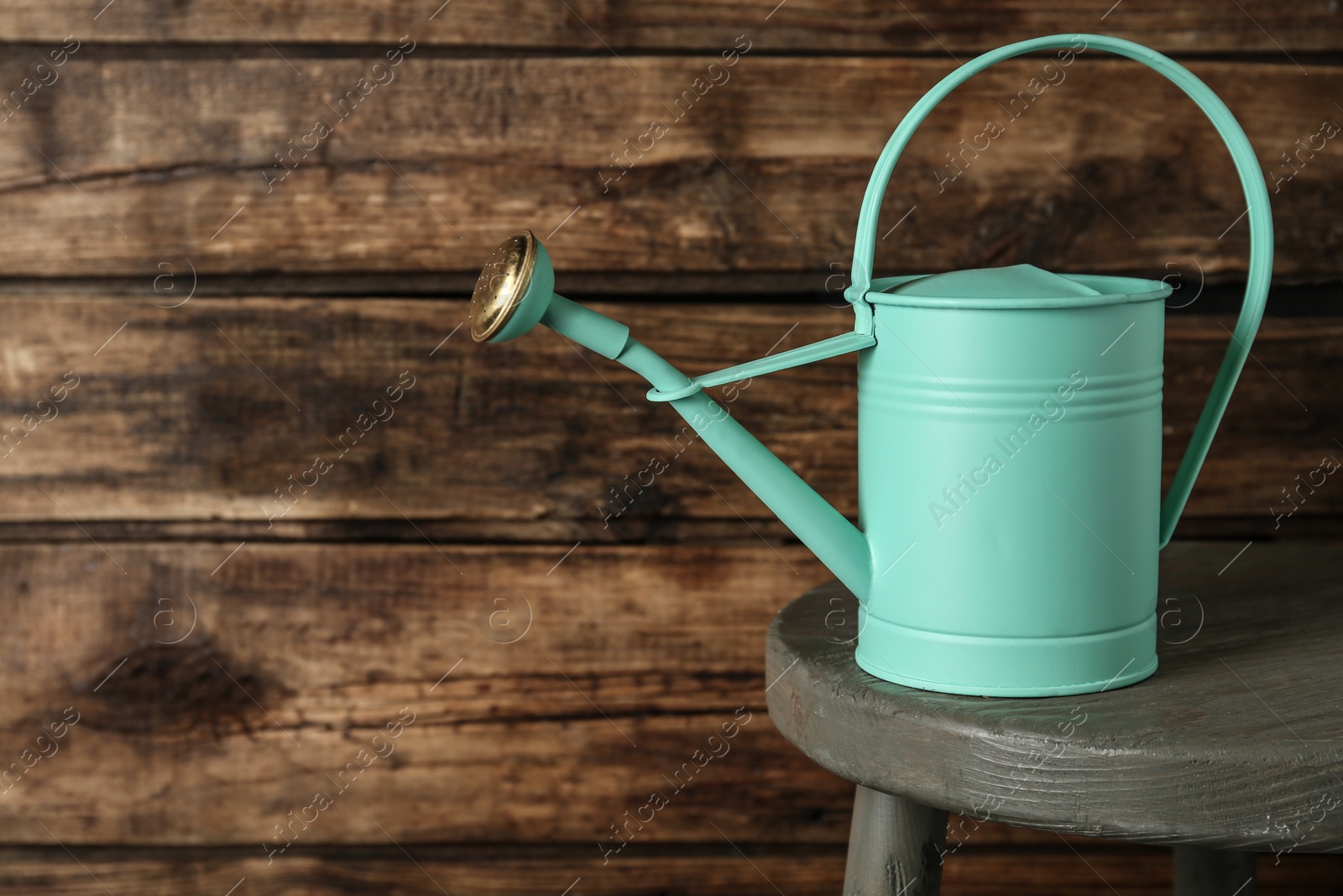 Photo of Turquoise metal watering can on table against wooden background, space for text