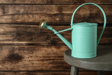 Turquoise metal watering can on table against wooden background, space for text