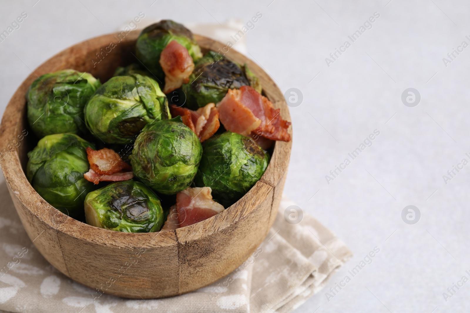 Photo of Delicious roasted Brussels sprouts and bacon in bowl on light table, closeup. Space for text