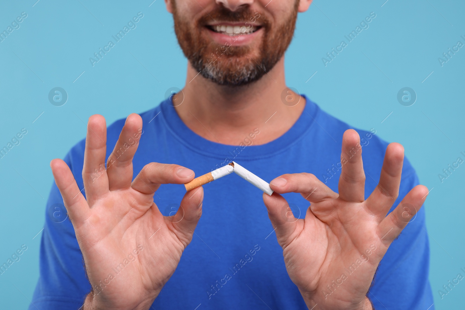 Photo of Stop smoking concept. Man breaking cigarette on light blue background, closeup