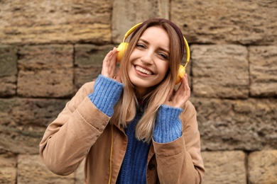 Photo of Young woman with headphones listening to music near stone wall
