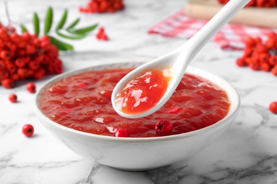 Photo of Delicious rowan jam in bowl and berries on white marble table, closeup