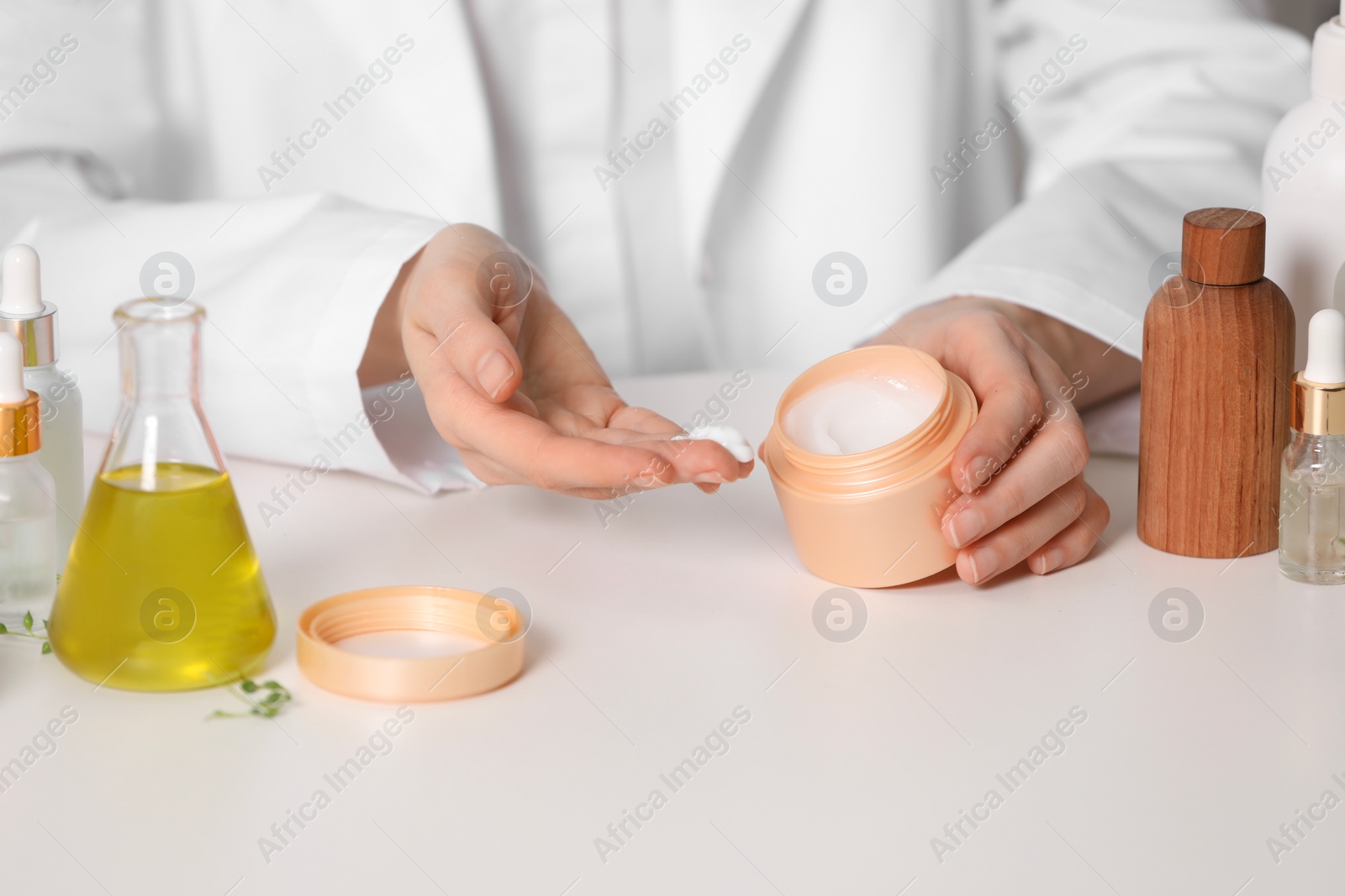 Photo of Dermatologist with jar testing cosmetic product at white table, closeup