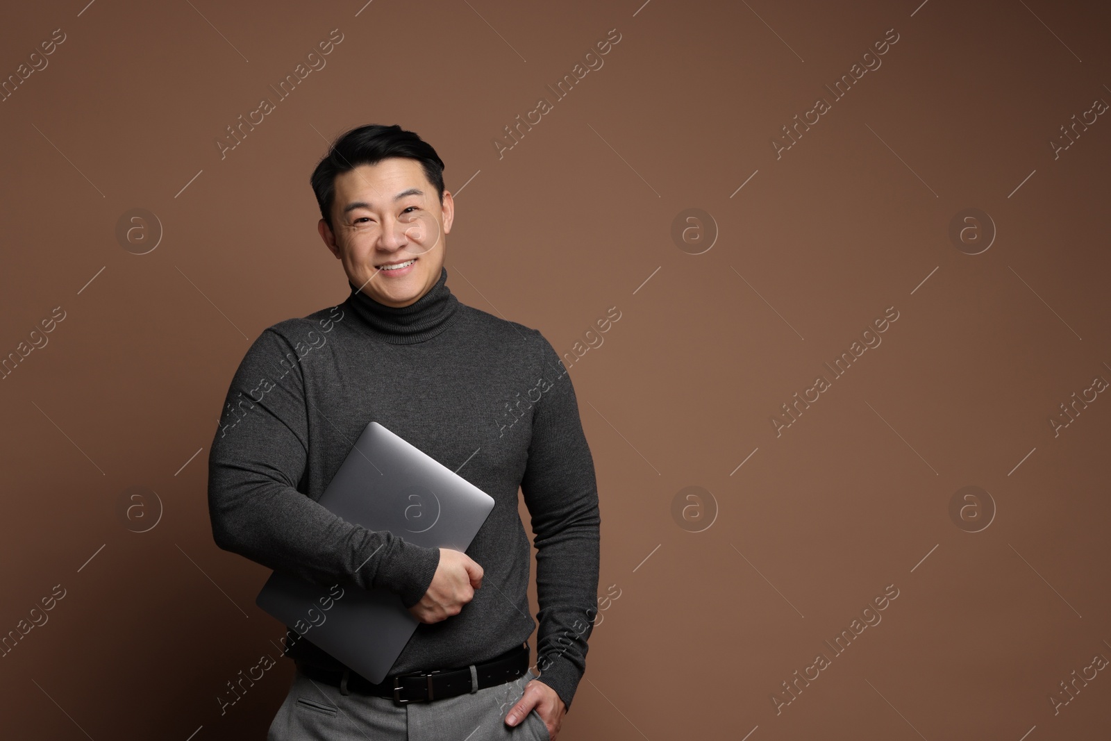 Photo of Portrait of happy man with laptop on brown background. Space for text