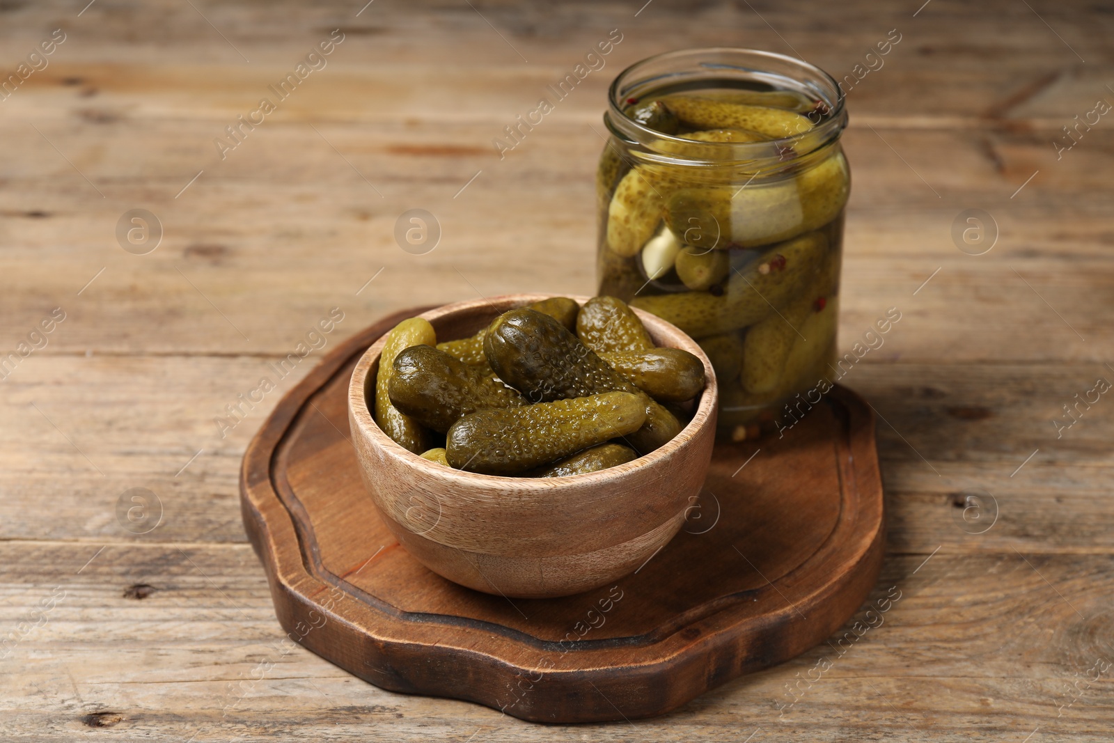 Photo of Tasty pickled cucumbers in jar and bowl on wooden table