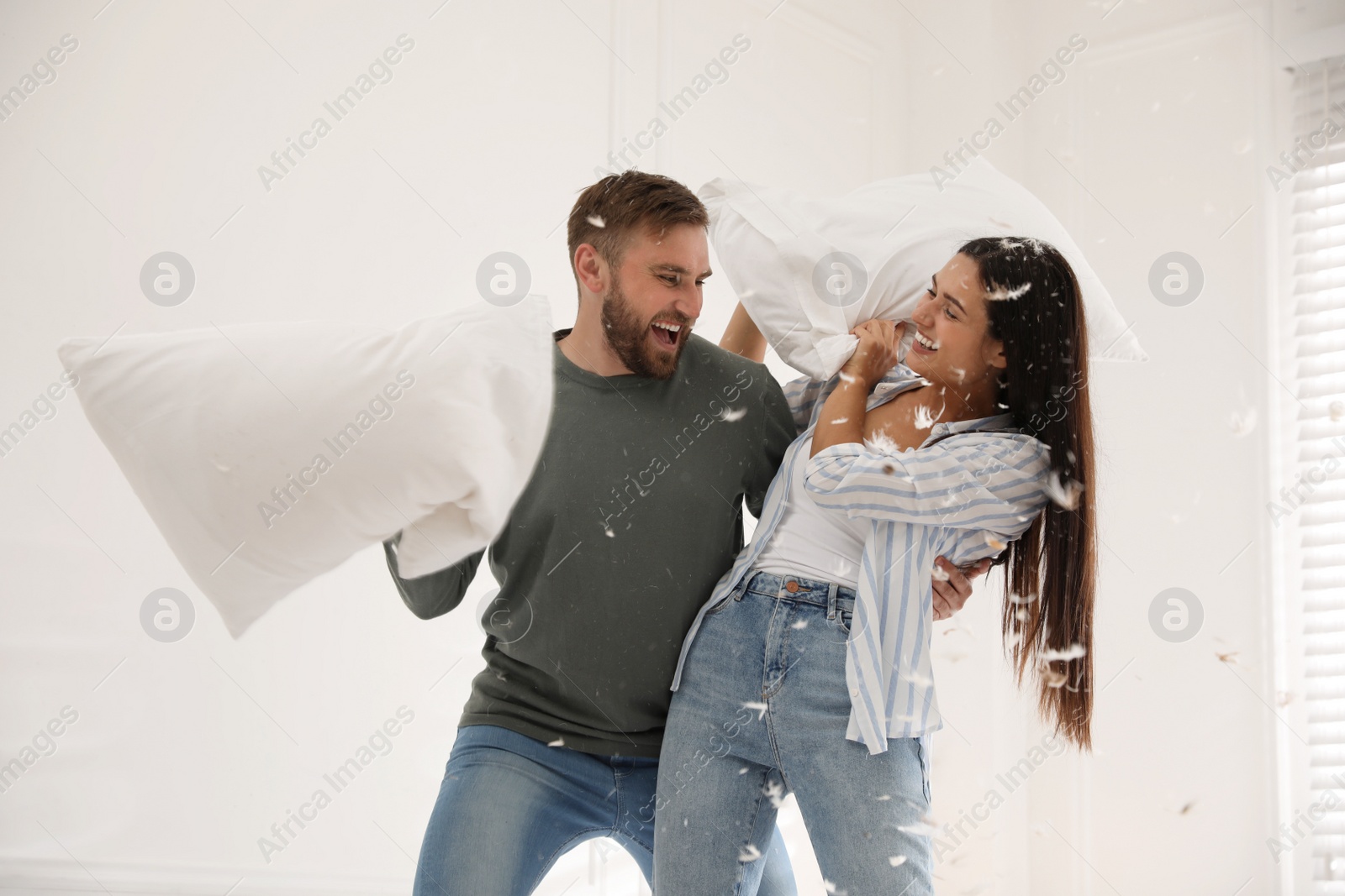 Photo of Happy young couple having fun pillow fight at home