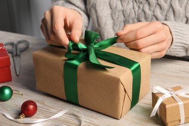 Woman decorating gift box at white wooden table, closeup. Christmas present