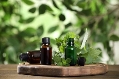 Photo of Glass bottles of nettle oil and leaves on wooden table against blurred background, space for text
