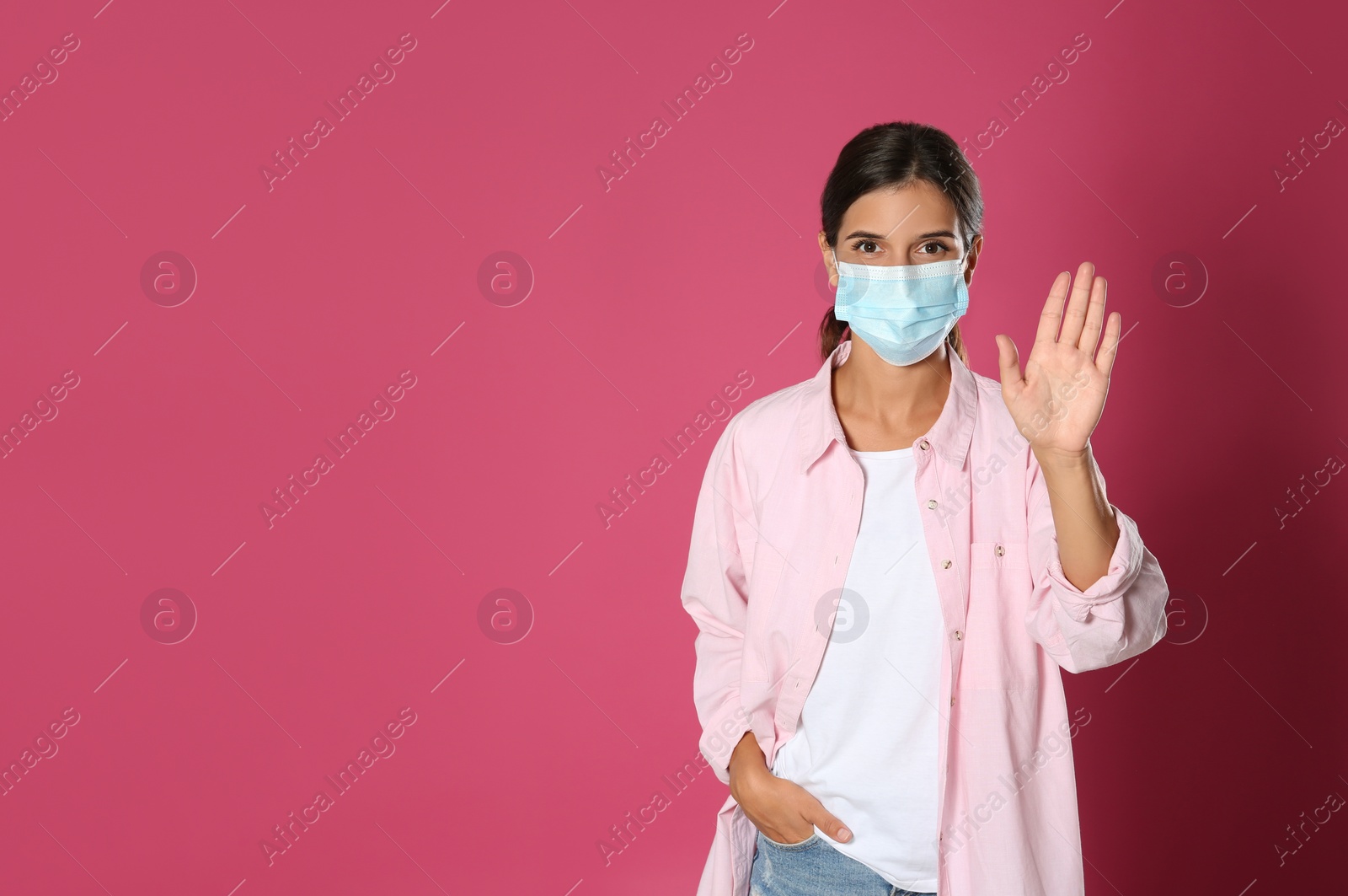 Photo of Woman in protective mask showing hello gesture on pink background, space for text. Keeping social distance during coronavirus pandemic