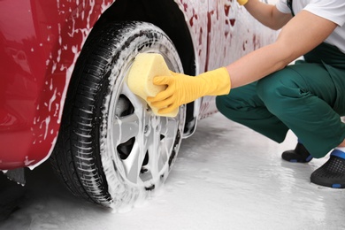 Photo of Male worker cleaning vehicle wheel with sponge at car wash