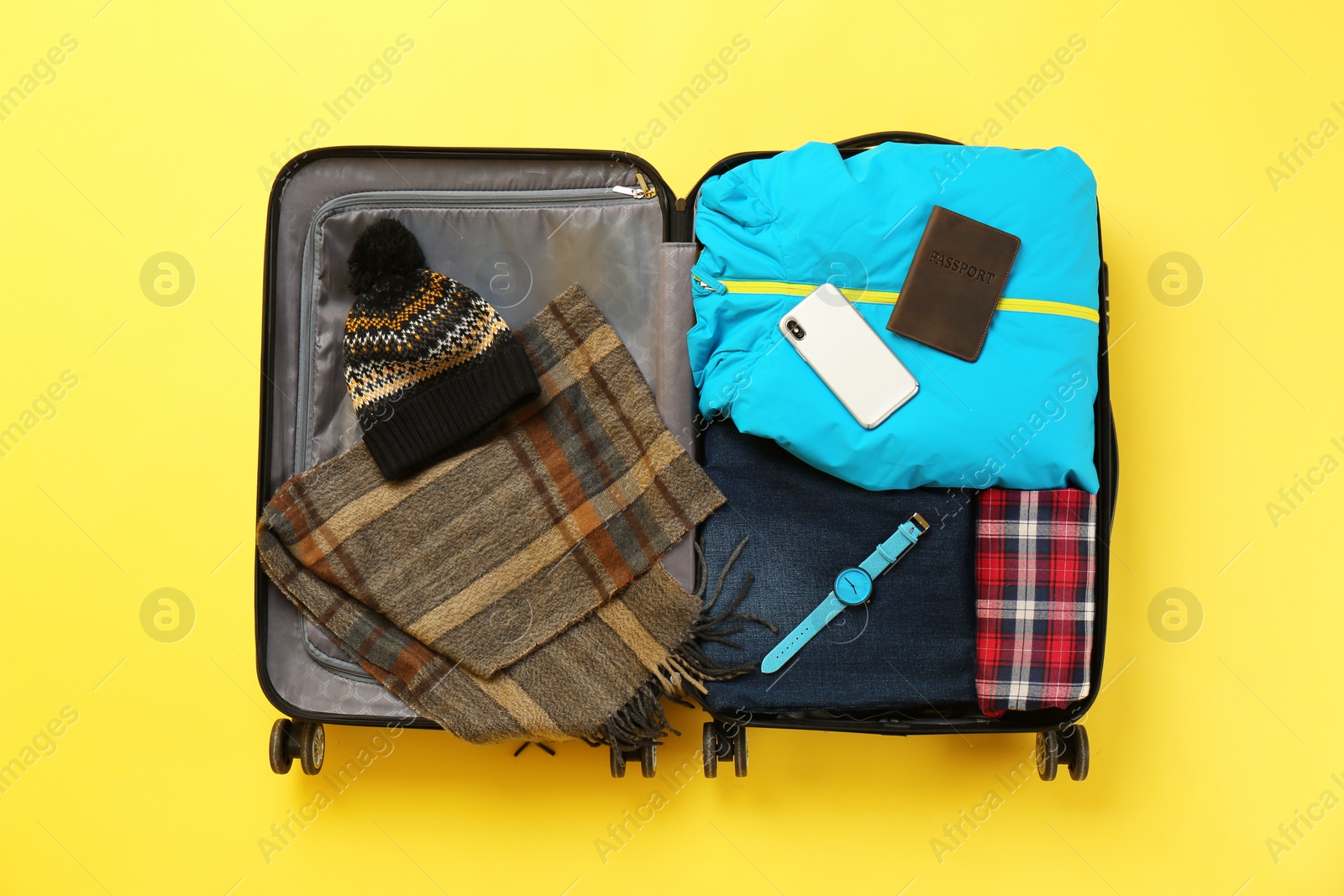 Photo of Open suitcase with warm clothes and accessories on color background, top view