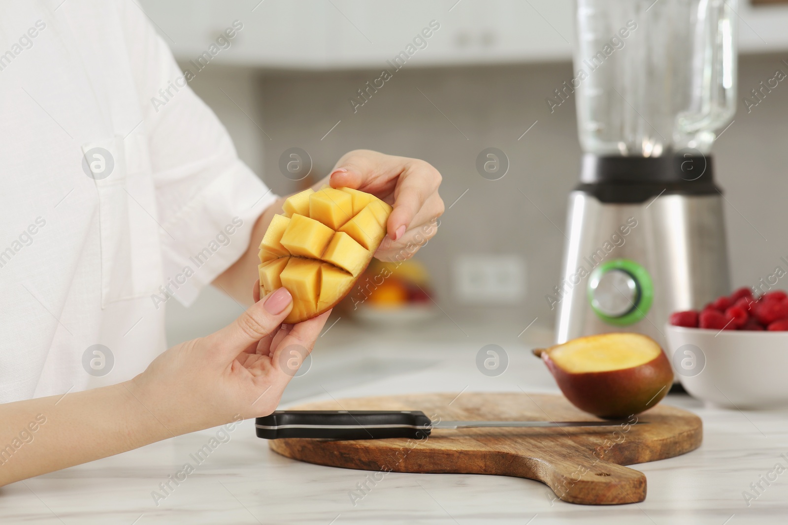 Photo of Woman preparing mango for tasty smoothie at white marble table in kitchen, closeup