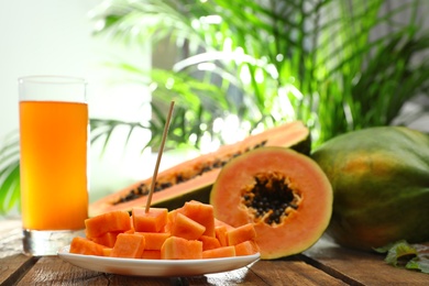 Photo of Fresh papayas and juice on wooden table against blurred background, space for text