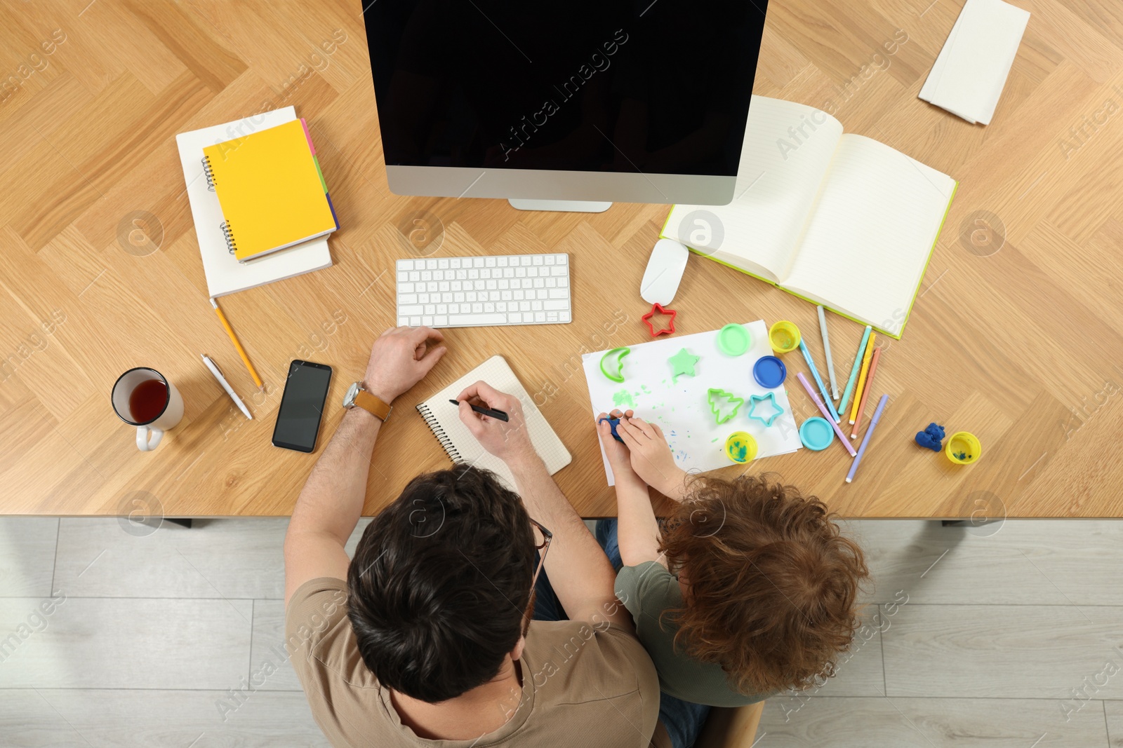 Photo of Man working remotely at home. Father and his son at desk with computer, top view