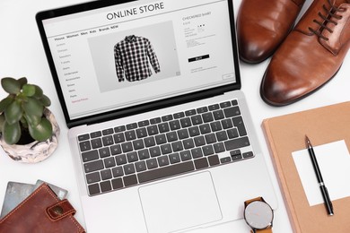 Photo of Online store website on laptop screen. Computer, stationery, credit cards, men's shoes and accessories on white background, above view