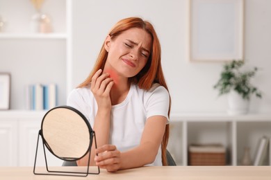 Suffering from allergy. Young woman with mirror scratching her face at home, space for text