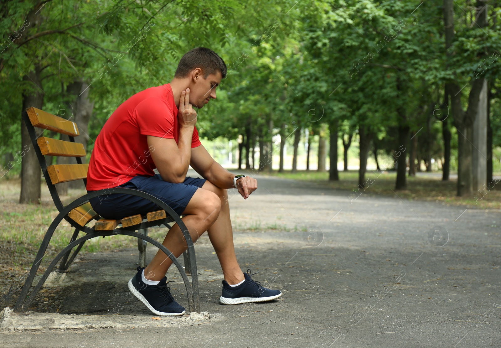 Photo of Young man checking pulse after training on bench in park. Space for text