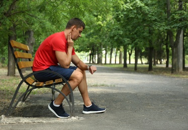 Photo of Young man checking pulse after training on bench in park. Space for text