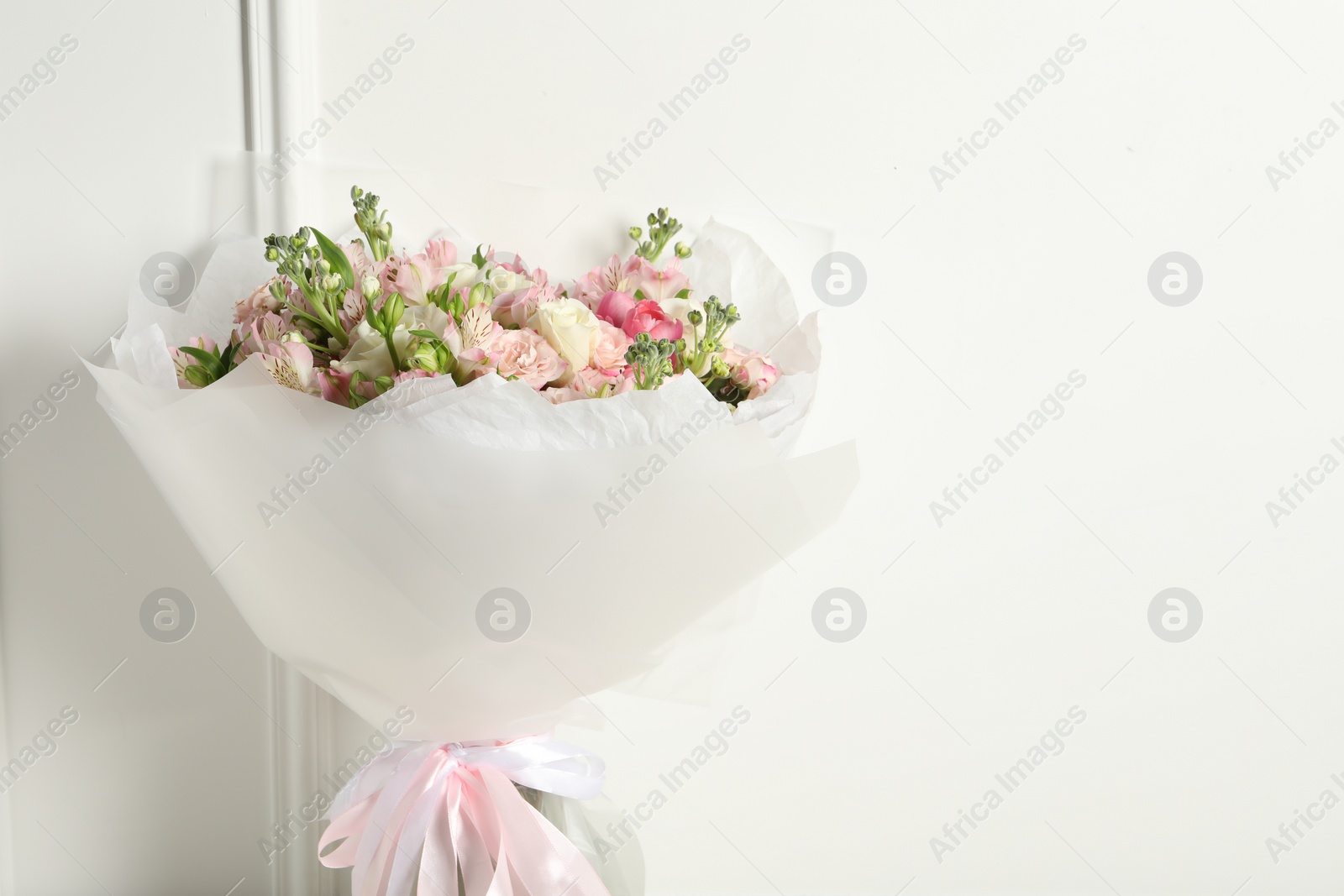 Photo of Beautiful bouquet of fresh flowers near white wall, space for text