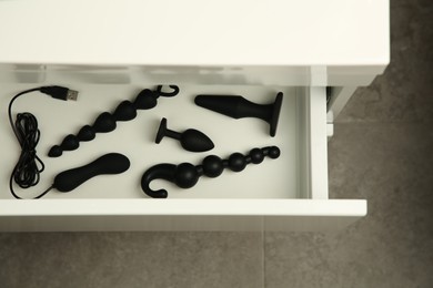 Photo of Black vibrator, anal plugs and beads in drawer indoors, top view. Sex toys
