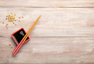 Soy sauce in bowl, soybeans and chopsticks on wooden table, flat lay. Space for text