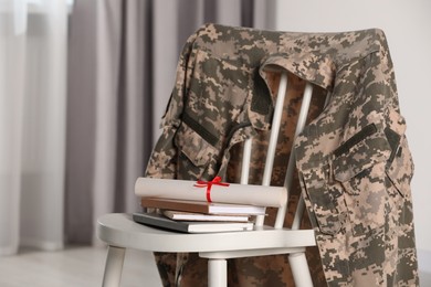 Photo of Chair with soldier uniform, notebooks and diploma indoors. Military education