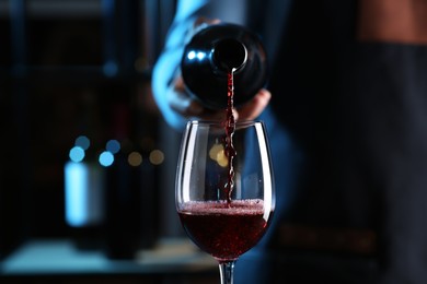 Photo of Bartender pouring red wine from bottle into glass indoors, closeup