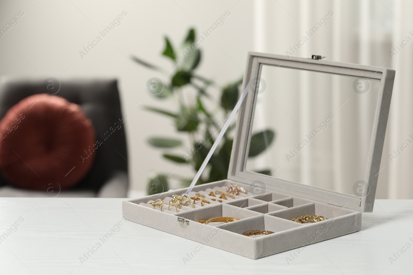 Photo of Jewelry box with different golden accessories on white wooden table indoors. Space for text