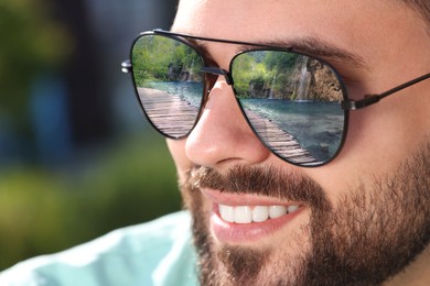 Image of Man in sunglasses on sunny day outdoors. Lake with wooden bridge reflecting in lenses