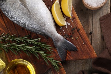 Photo of Raw dorado fish, lemon wedges and spices on wooden table, flat lay