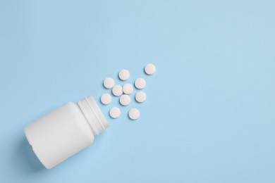 Plastic medical bottle with pills on light blue background, flat lay. Space for text