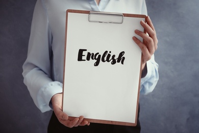 Photo of Woman holding clipboard with word English on grey background, closeup