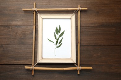 Photo of Bamboo frame with dried plant on wooden table, top view