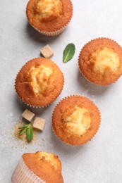 Delicious sweet muffins and brown sugar on light grey textured table, flat lay