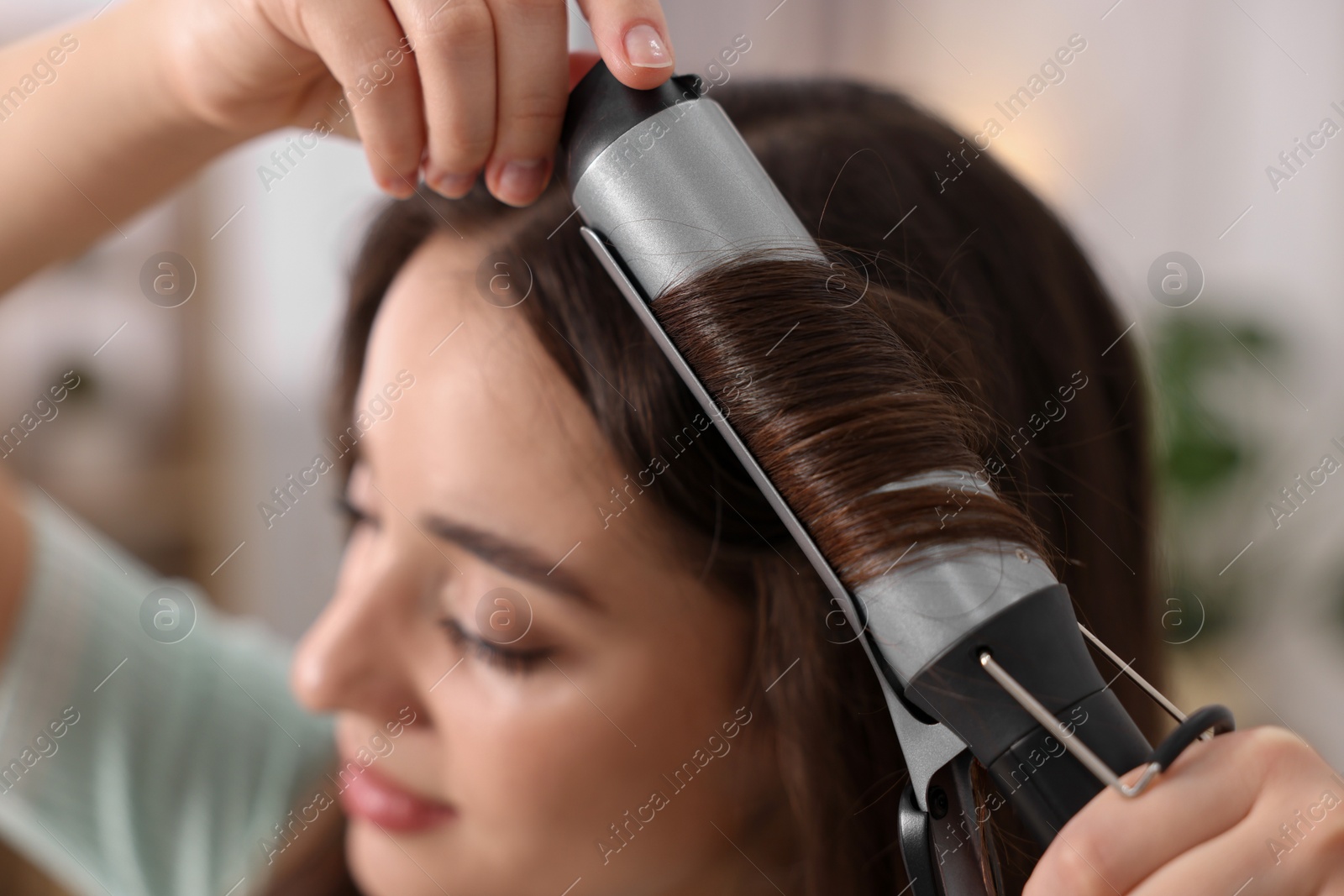 Photo of Woman using curling hair iron indoors, selective focus