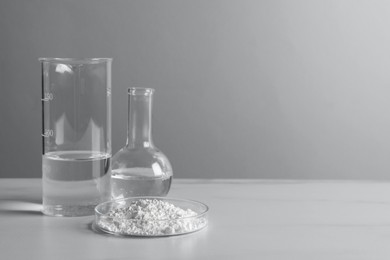 Photo of Petri dish with calcium carbonate powder and laboratory glassware on white table. Space for text