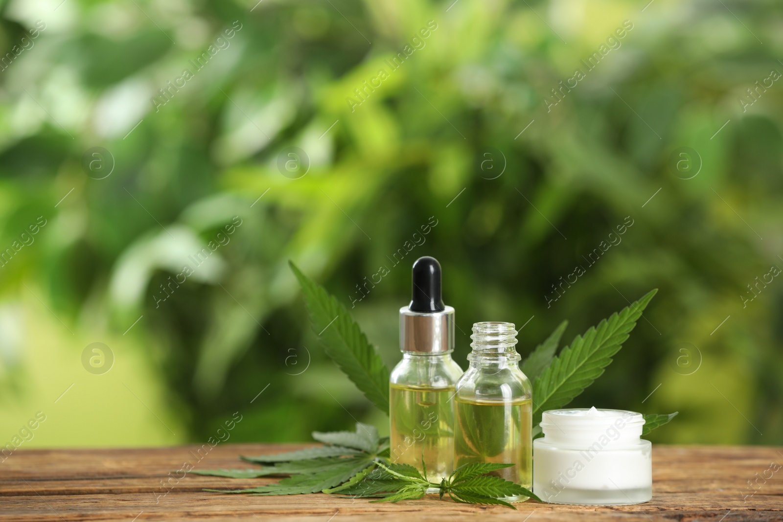 Photo of Cream, hemp leaves, bottles of CBD oil and THC tincture on wooden table. Space for text