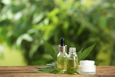 Photo of Cream, hemp leaves, bottles of CBD oil and THC tincture on wooden table. Space for text