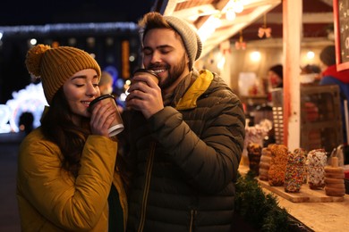 Photo of Lovely couple with cups of hot drinks spending time together at Christmas fair