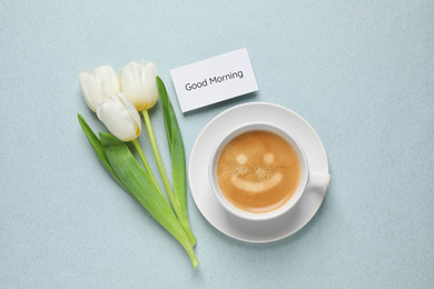 Image of White tulips, coffee and card with Good morning wish on light blue background, flat lay